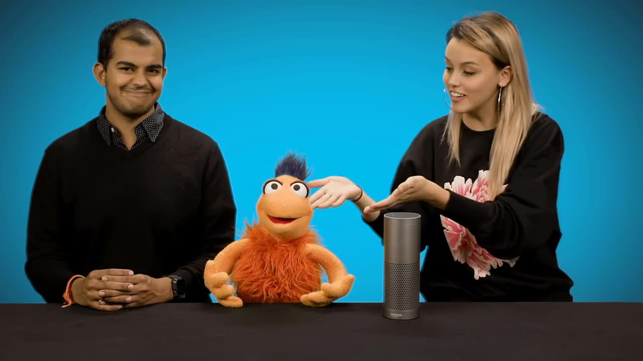 Akersh and Cami at a desk with Sylvester, a small orange puppet, and an Echo speaker
